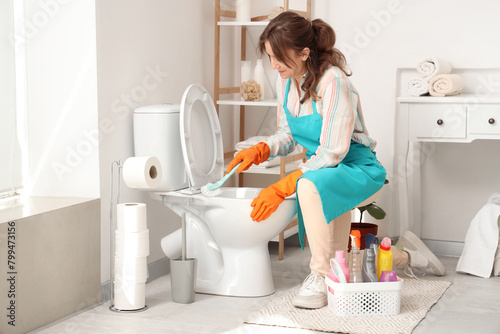 Young woman cleaning toilet bowl with brush in light bathroom photo