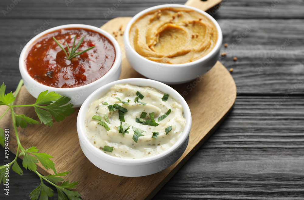 Different tasty sauces in bowls and parsley on black wooden table, closeup Different tasty sauces in bowls and parsley on black wooden table, closeup