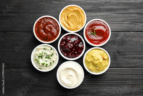 Different tasty sauces in bowls on black wooden table, flat lay
