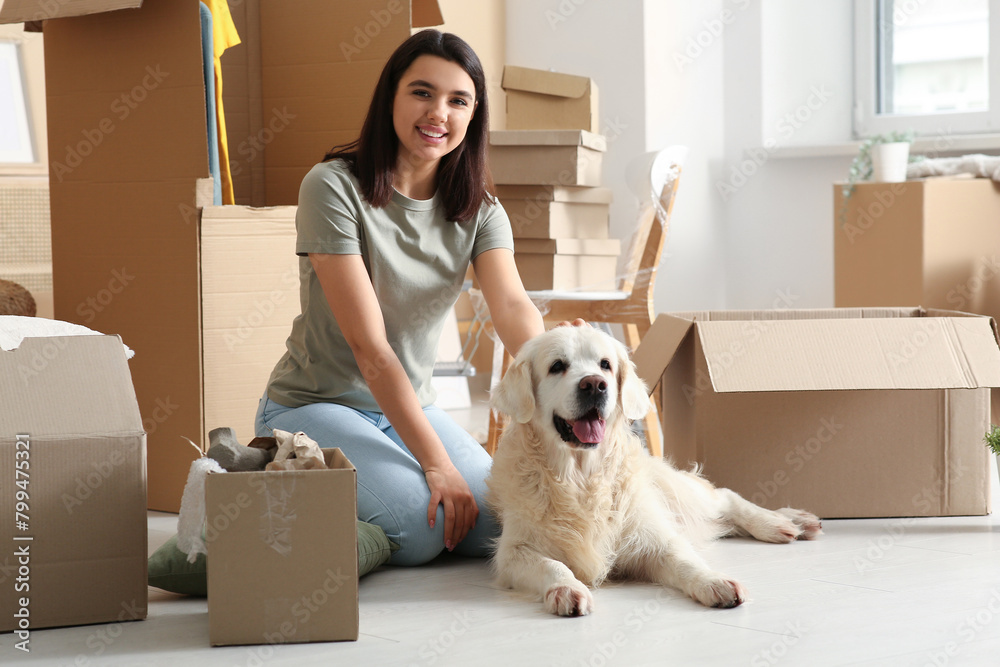 Fototapeta premium Young happy woman and cute Labrador dog with boxes on moving day sitting at home