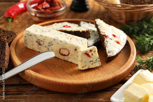 Tasty butter with dill, chili pepper and rye bread on wooden table