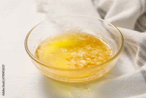 Melted butter in glass bowl on white wooden table, closeup