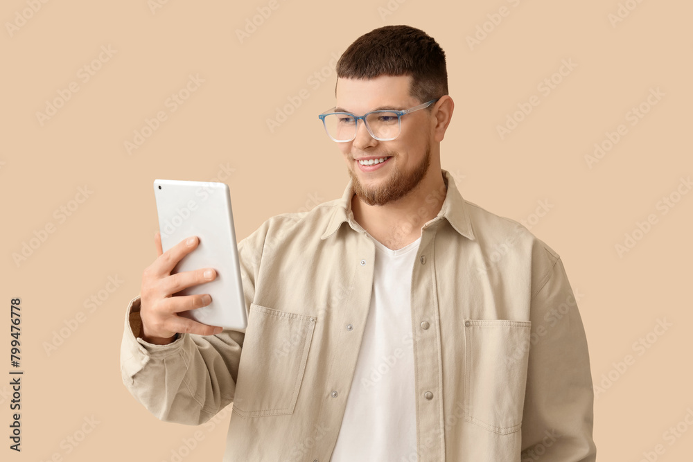 Young man in eyeglasses using tablet computer on beige background Young man in eyeglasses using tablet computer on beige background
