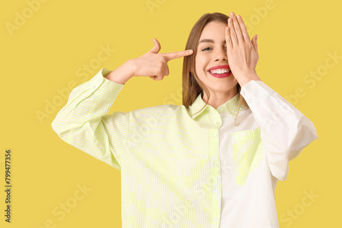 Young woman checking her eyesight on yellow background