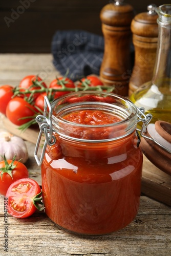 Homemade tomato sauce in jar and fresh ingredients on wooden table, closeup