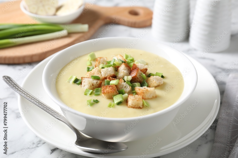 Tasty potato soup with croutons in bowl and spoon on white marble table