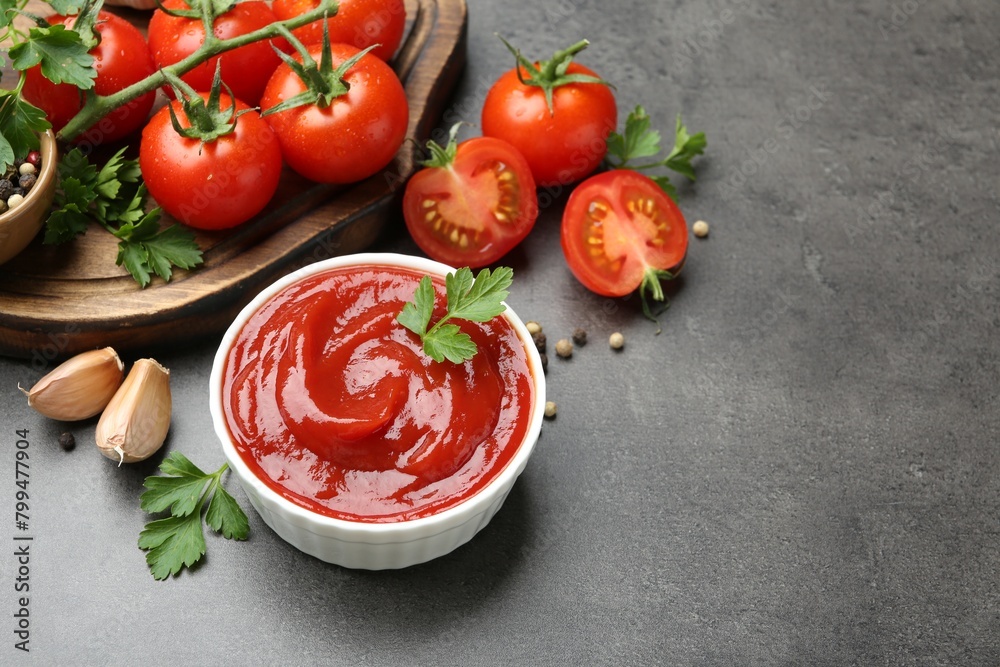 Delicious ketchup in bowl, tomatoes, parsley and garlic on grey table, closeup. Space for text Delicious ketchup in bowl, tomatoes, parsley and garlic on grey table, closeup. Space for text