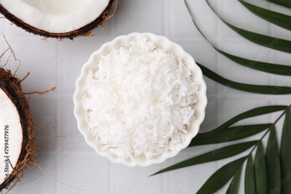 Coconut flakes in bowl, nuts and palm leaf on white tiled table, flat lay Coconut flakes in bowl, nuts and palm leaf on white tiled table, flat lay