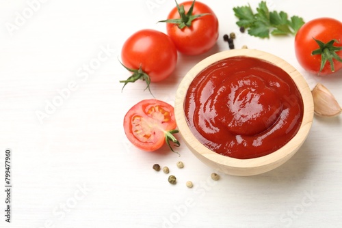 Delicious ketchup in bowl, peppercorns and tomatoes on white wooden table, above view. Space for text