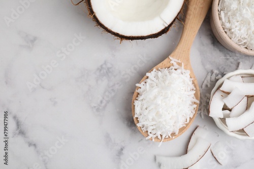 Coconut flakes, nut and spoon on white marble table, flat lay. Space for text