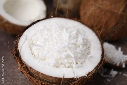Coconut flakes in nut shell on brown table, closeup