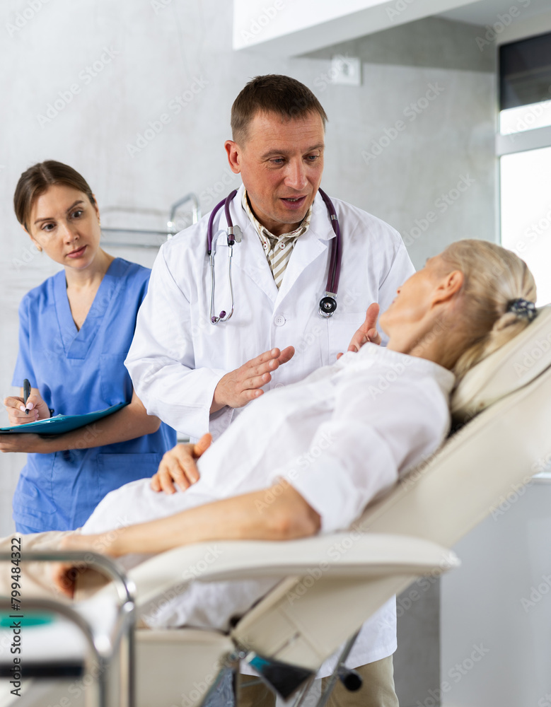 Fototapeta premium Male beautician, together with a nurse, examines the face of an elderly woman and plans facelift procedures.