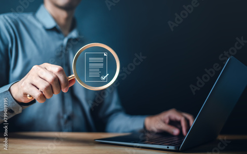 document, job, keyboard, management, marketing, report, research, information, search, file. A man is holding a magnifying glass over a laptop screen. possibly related to work or research. © Day Of Victory Stu.