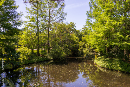 a beautiful spring landscape in the Sculpture Garden at New Orleans City Park with a lake, lush green trees, grass and plants, sculptures, people and blue sky in New Orleans Louisiana USA
