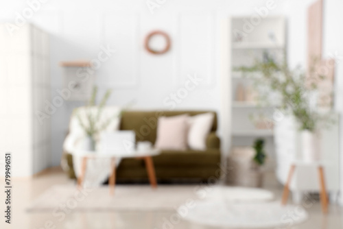Stylish room with green sofa, coffee table and blooming branches, blurred view
