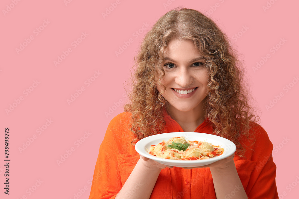 Happy young woman with plate of tasty ravioli on pink background