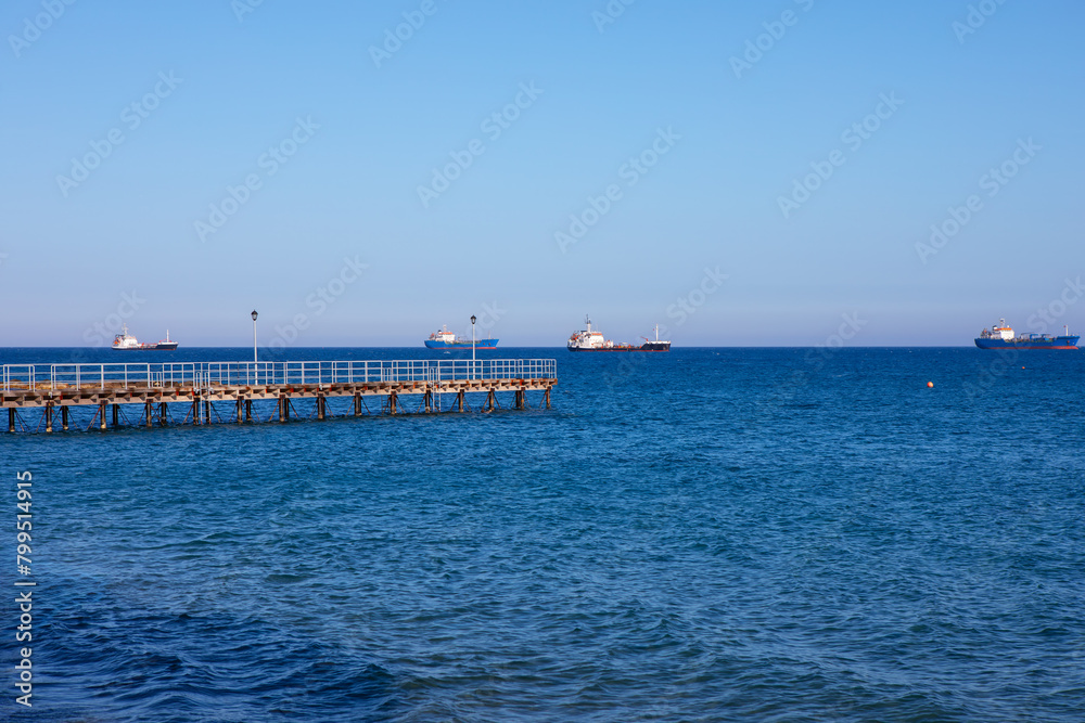 Pier in the sea with ships in the distance on the horizon. Blue sky over blue sea 