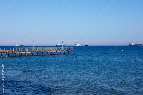 Pier in the sea with ships in the distance on the horizon. Blue sky over blue sea 