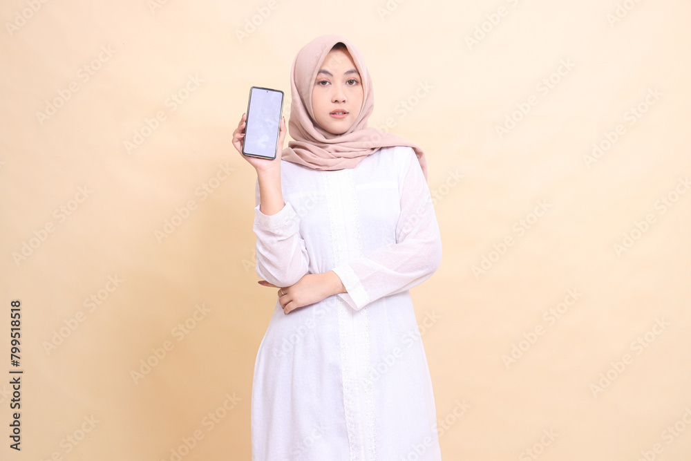 Portrait of an Asian Muslim woman wearing an elegant hijab holding a cellphone gadget in her hand and holding her arms up. Lifestyle, business and finance concept Portrait of an Asian Muslim woman wearing an elegant hijab holding a cellphone gadget in her hand and holding her arms up. Lifestyle, business and finance concept