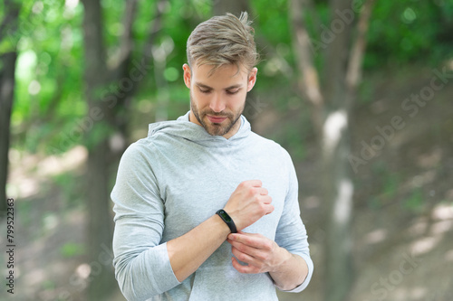 Sporty fit man with sport equipment checks time on smartwatch. Man tracking fitness results dressed in sportswear outdoor. Man runner with fitness gadget. Smartwatch for fitness photo
