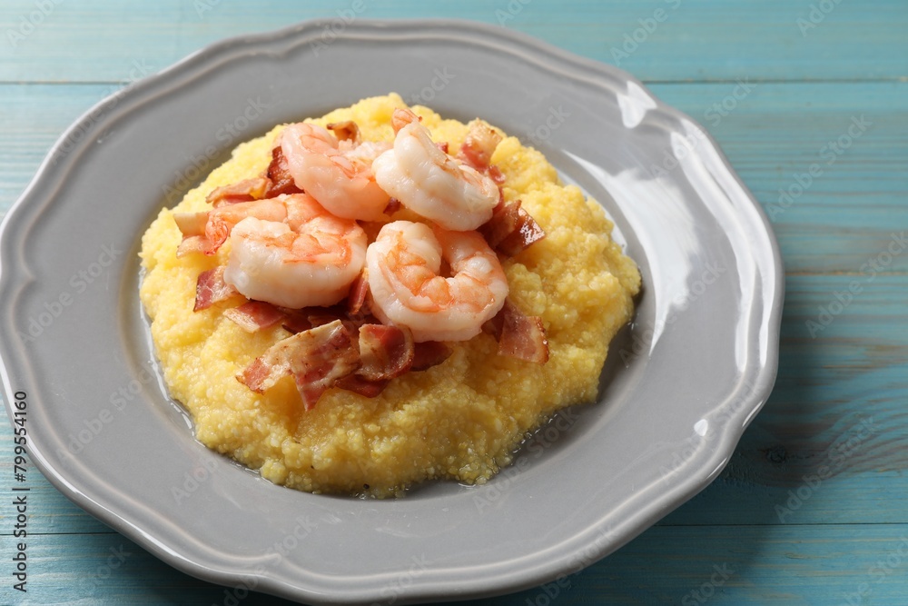 Plate with fresh tasty shrimps, bacon and grits on light blue wooden table, closeup