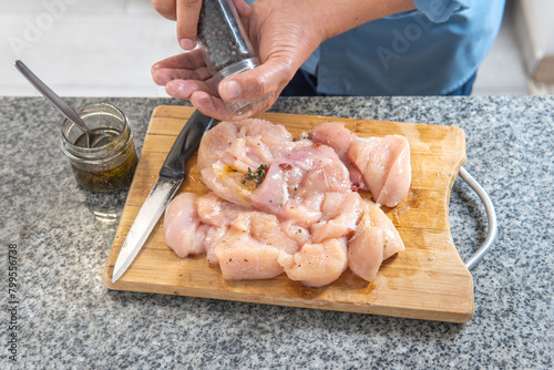 Man's hands seasoning raw chicken with pepper.