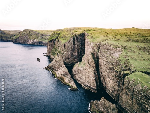 Aerial shot of ocean and coast with huge cliffs and green field