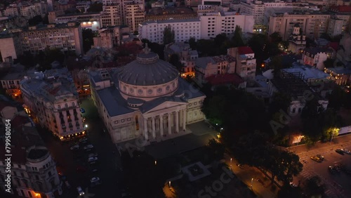 4k drone footage. Camera flies up revealing a view of the Romanian Athenaeu, a concert hall in the center of Bucharest. One of the main landmarks of the Romanian capital. Evening city lights at dusk photo