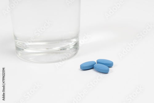 Blue pills for treating erectile dysfunction on a white table with glass of water. Close up.