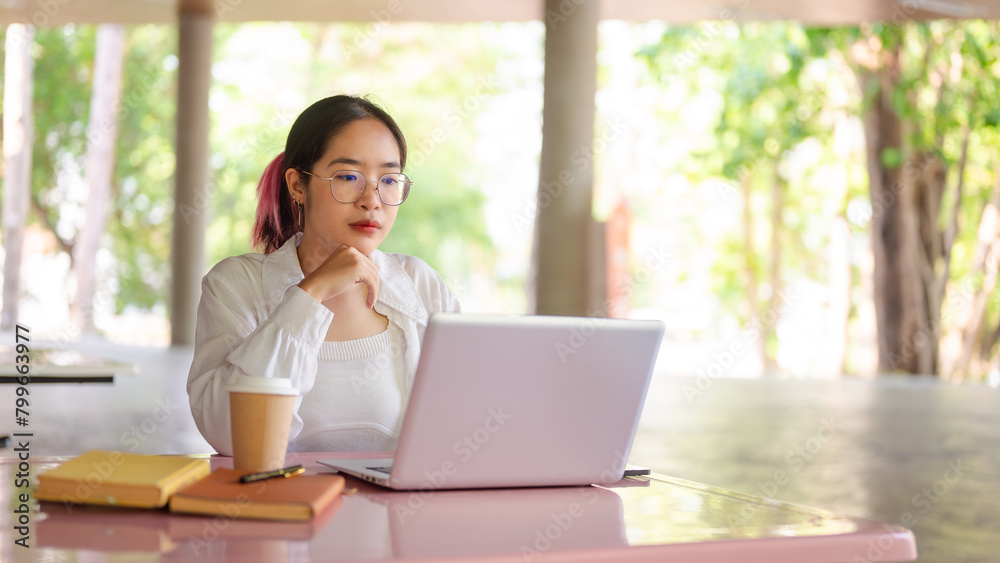 A focused female student working on her laptop while sitting at a table in her college cafeteria. A focused female student working on her laptop while sitting at a table in her college cafeteria.