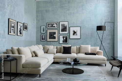 A contemporary living room with a sky-blue brushed wall texture. The room features a modular sectional sofa in beige, a glass top side table, and a minimalistic black floor lamp