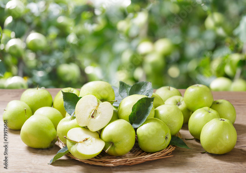 Green apples with leaves on wooden table on orchard garden background
