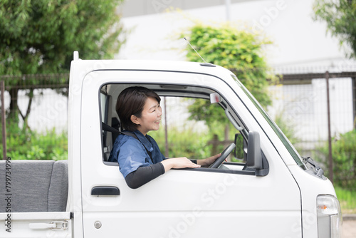 新緑の中トラックを運転する中年の作業着の女性の横顔 運送や配送業などのイメージ 廃品回収