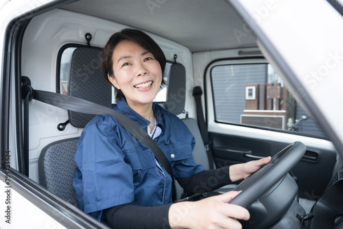 トラックを運転する中年の作業着の女性 カメラ目線 運送や配送業などのイメージ