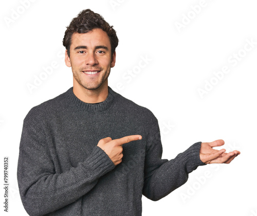 Young Hispanic man in studio excited holding a copy space on palm.