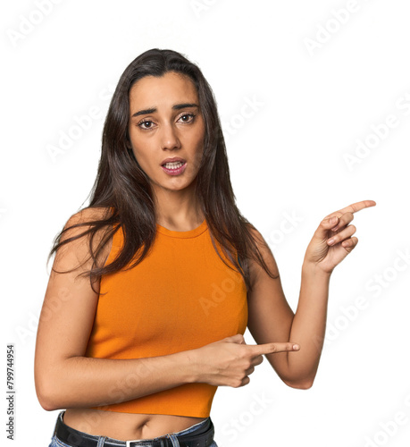 Hispanic young woman shocked pointing with index fingers to a copy space.