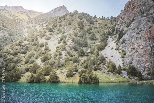 Mountain panorama, landscape with rocky peaks and blue turquoise lake Chukurak in the Fan Mountains in Tajikistan, hills covered with forest on a sunny summer day photo