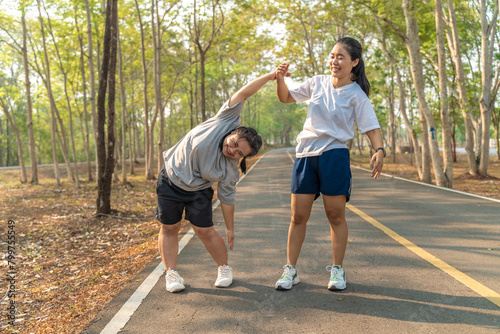 Two young female friends stretching their arms and legs before starting their morning run at a local running park