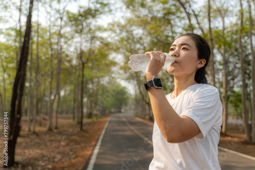 Young woman drinking water from a plastic bottle after her morning run at a local running park