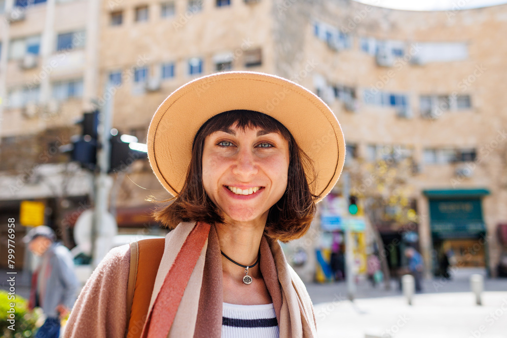 Close-up portrait of a cheerful white woman in a hat against the backdrop of the city in sunny weather. Weekend trip.