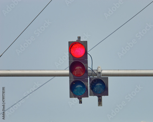 Close-up photo of a red traffic light on a metal pole with a clear blue sky in the background