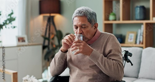 Senior man, wheelchair and drinking water in home with depression, sick or stress in retirement. Glass, house and elderly person with a disability, disease or frustrated with parkinson in living room photo