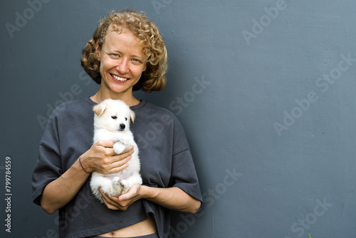 Portrait of a girl with a puppy, a woman of European appearance with curly hair holds a cute white puppy in her arms.
