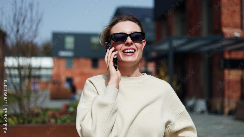 Satisfied female in stylish sunglasses strolling along street while having chat with boyfriend on phone. Happy woman in great mood communicating on smartphone while walking and enjoying sunny day. Satisfied female in stylish sunglasses strolling along street while having chat with boyfriend on phone. Happy woman in great mood communicating on smartphone while walking and enjoying sunny day.
