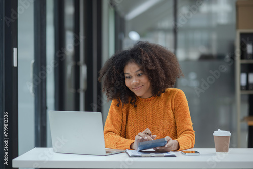 African American female working with laptop and calculator at desk in office.