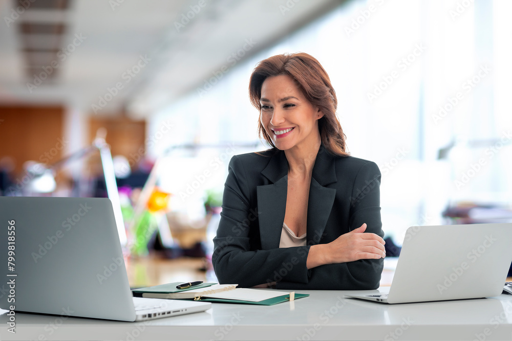 Mid aged businesswoman sitting at the office and having video call Mid aged businesswoman sitting at the office and having video call