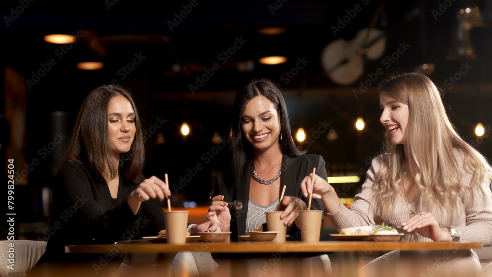 A group of beautiful women talking and having fun together in a restaurant in the evening. A group of girlfriends enjoying food and having fun. Lifestyle concept with happy women on the terrace.