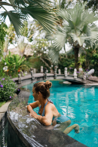 Beautiful young woman model in back bikini lies in swimming pool, posing and tanned on summer vacation. Healthy body care