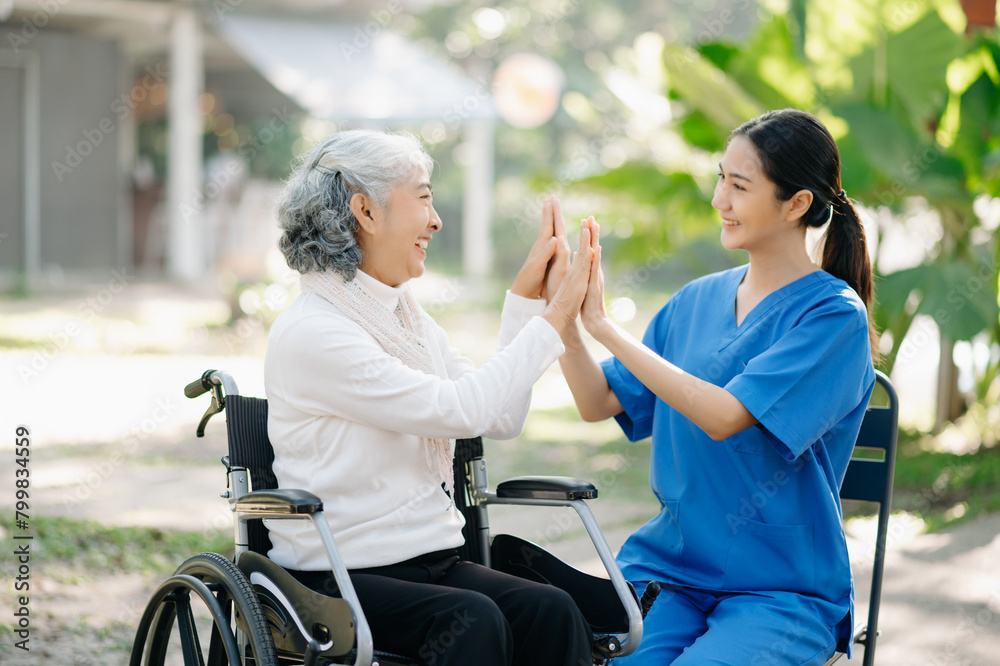 Elderly asian senior woman on wheelchair with Asian careful caregiver and encourage patient, walking in garden. with care from a caregiver Elderly asian senior woman on wheelchair with Asian careful caregiver and encourage patient, walking in garden. with care from a caregiver
