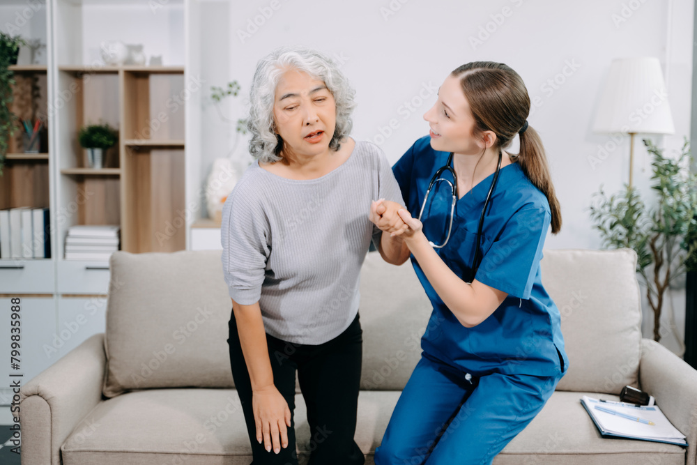 Obraz premium Young nurse helping elderly woman walk in the room, holding his hand, supporting. Treatment and rehabilitation after injury in assisted living facility.